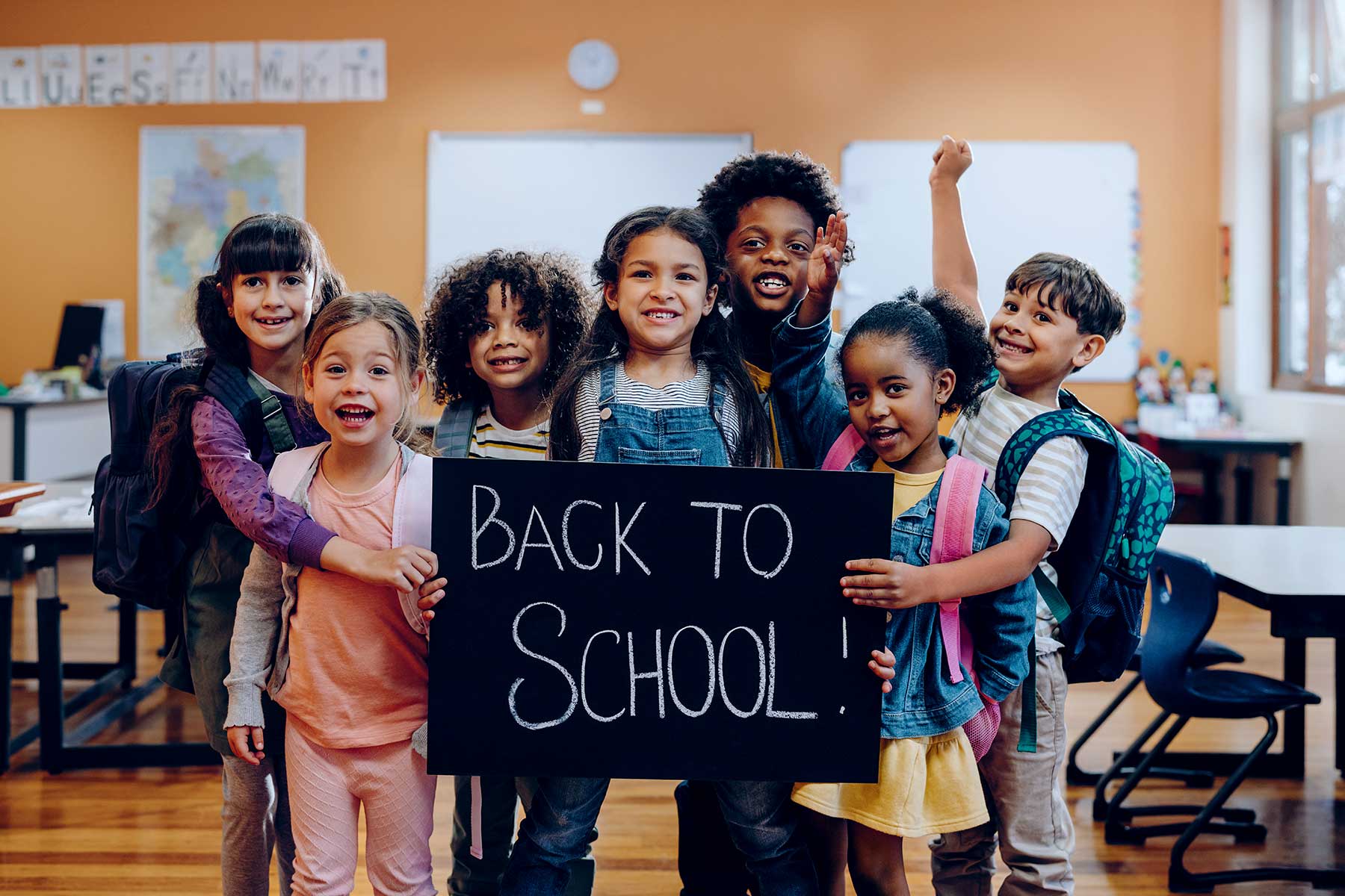 Children in a classroom, happy and holding a back to school sign in chalkboard style